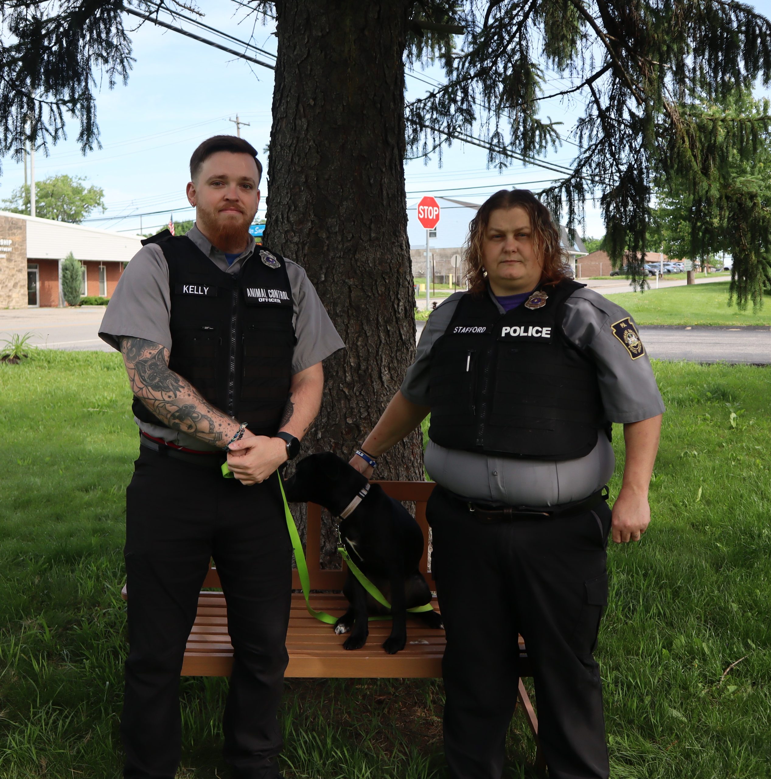 Animal Control Officer Jon Kelly and Humane Society Police Officer Wendi Stafford standing with a dog between them under a tree.